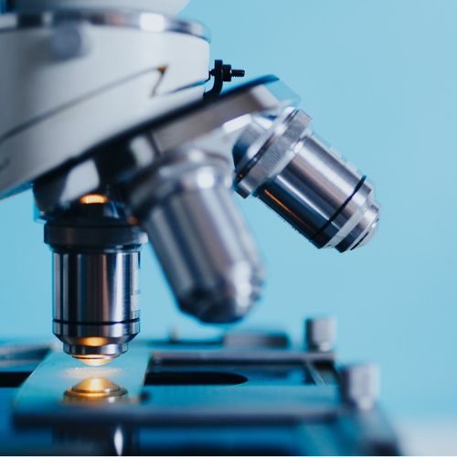 A close-up of a microscope with multiple lenses, poised over a slide, showcasing a scientific instrument used for magnifying objects, set against a pale blue background suggesting a laboratory setting