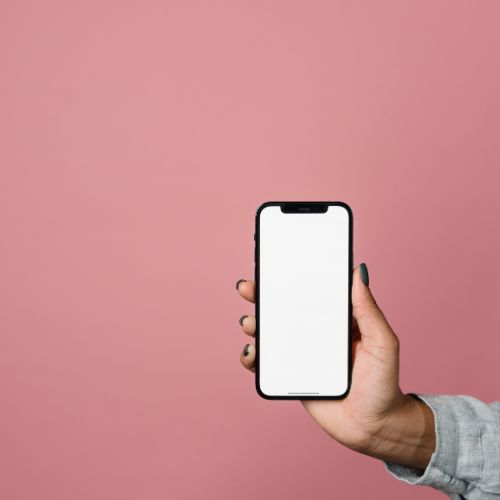 A hand holding a smartphone with a blank white screen against a pink background, indicating a mockup for design presentation, mobile application demonstration, or connectivity concept.