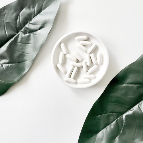 A minimalist composition featuring a white plate with white capsules on it, flanked by two large green leaves, evoking a clean, medical aesthetic that could suggest the presence of Monolaurin supplements, known for their immune support benefits.