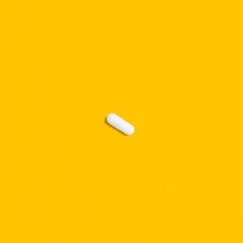A single white oblong tablet centered on a vibrant yellow background, presenting a minimalist pharmaceutical concept