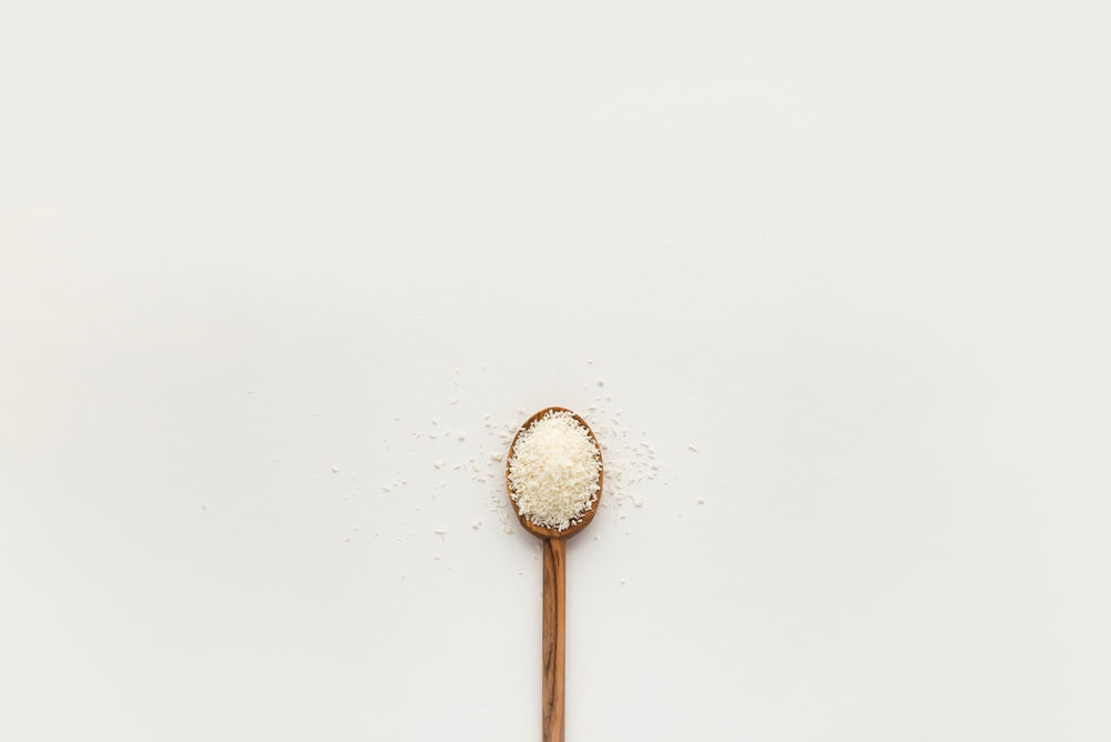 A minimalistic image of a wooden spoon filled with Monolaurin, centered on a plain white background with some powder sprinkled around.