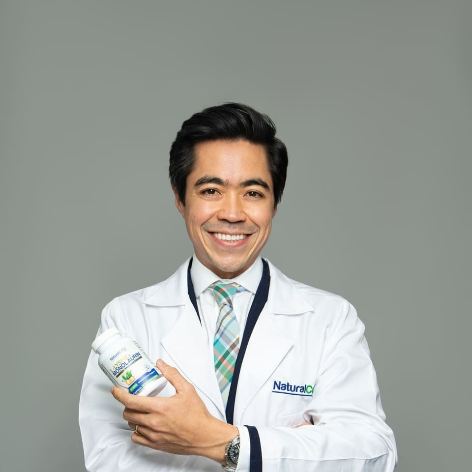 Damon Sununtnasuk, founder and CEO of Natural Cure Labs, in a white lab coat holding a bottle of L-Lysine with Monolaurin