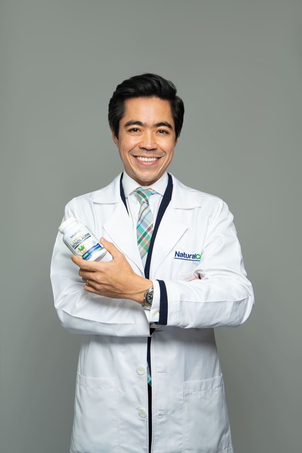 Damon Sununtnasuk, founder of Natural Cure Labs, in a white lab coat holding a bottle of L-Lysine with Monolaurin